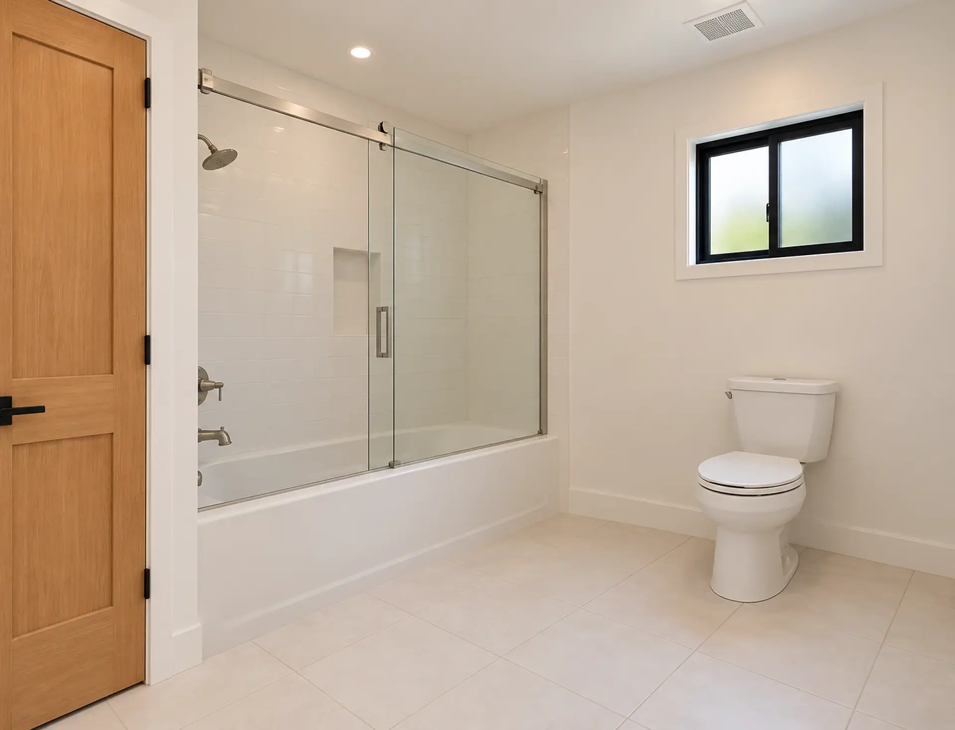 Rendering of the ADU 1200 hall bath: a white tub with a tiled shower and a glass sliding door across the far end, the toilet under a small black-framed window with frosted glass, and the light-oak door on the left.